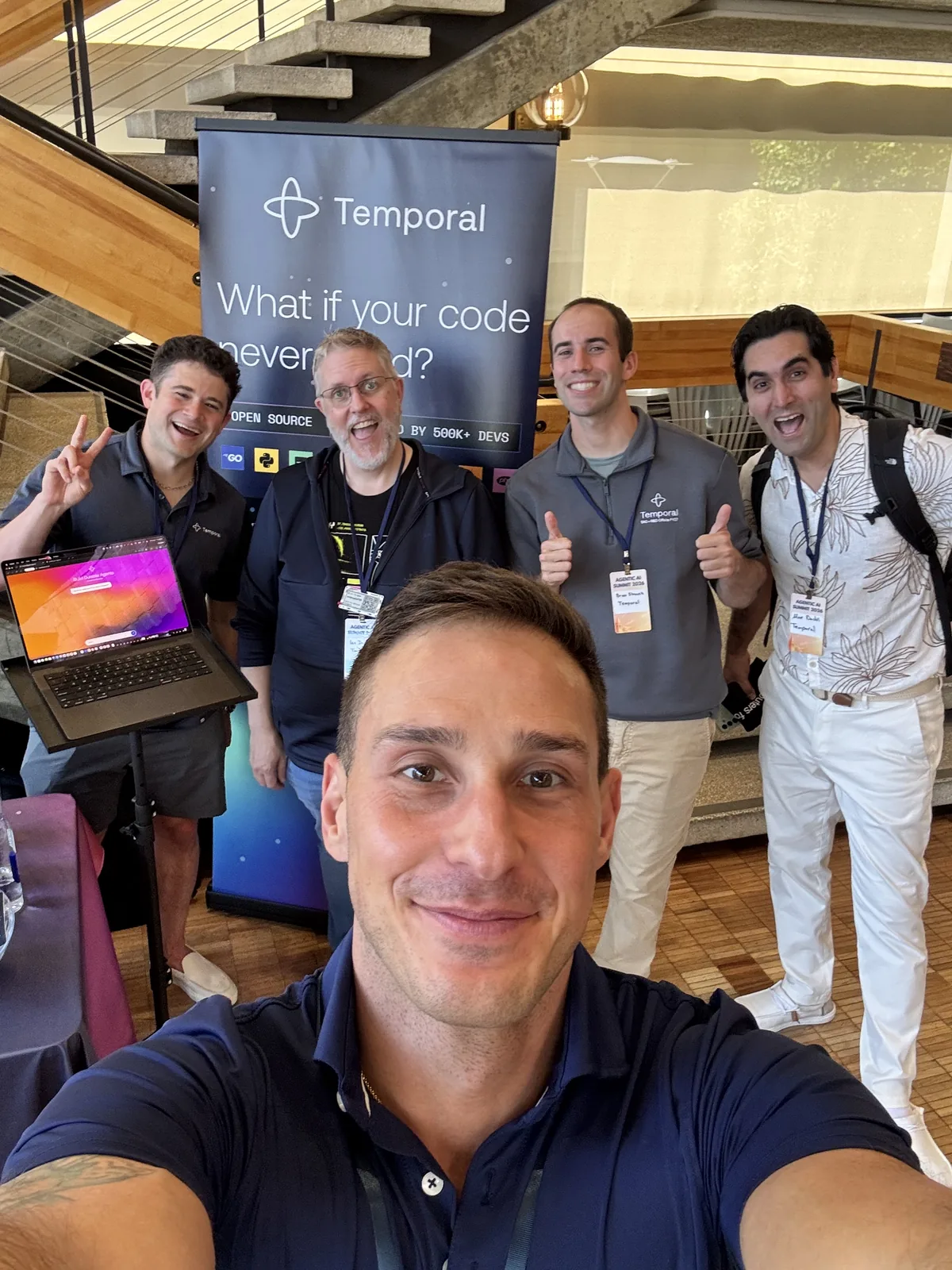 Nikolay taking a selfie with four Temporal colleagues beside a Temporal banner reading 'What if your code never failed?'